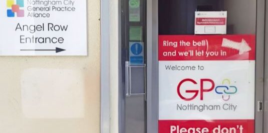 Entrance doorway with red 'Ring the bell and we'll let you in' sign and 'Please don't push the door' warnings; Nottingham City GP welcome sign nearby.
